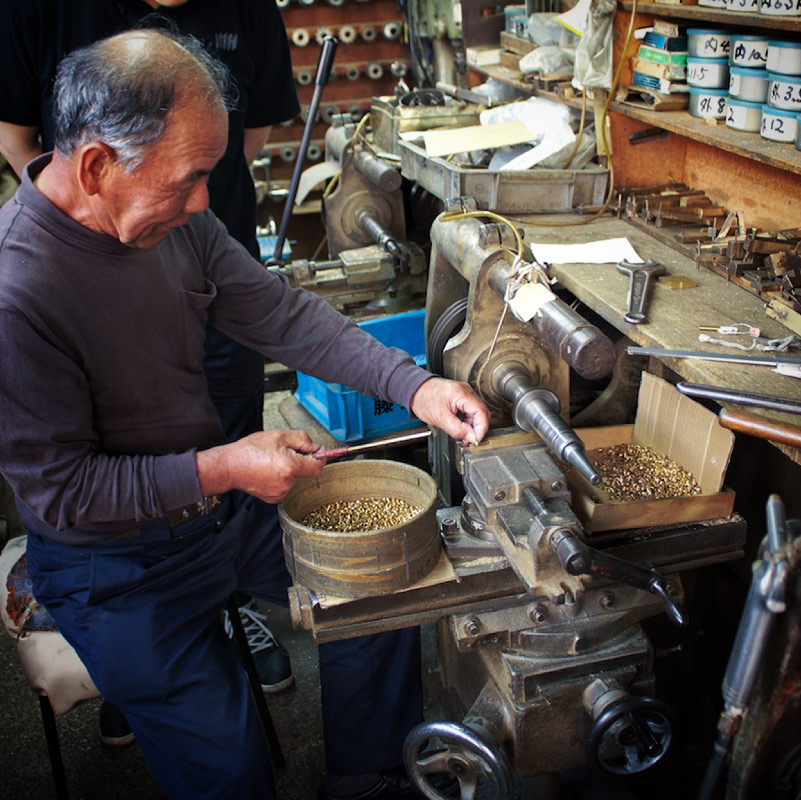“挽き物職人” 金属を切断、彫刻、削り、穴あけ、ねじ切りに特化した技術。挽き物とは金属を挽いて、金具を切り出したり、金属に溝を彫ったり、作ったりする技。真鍮の板材、丸材をメインの素材として扱い、デザインや図面に合わせて形を成形していく、１９２０年代から続く、古くからある日本の伝統技術。
