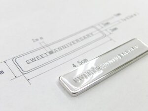 通常であれば、個別のネームやロゴ、シリアルナンバー、ホテルのルームキーなどのナンバリングを製作するのに一つ一つ職人が手彫りにて彫刻する為に高額な費用が必要になりますが、メタルハウスでは、特殊な化学技術を使用することで、真鍮板に直接個別な文字や数字、部屋番号などを、費用を可能な限り軽減しながら、お客様のイメージを金具にする事ができます。